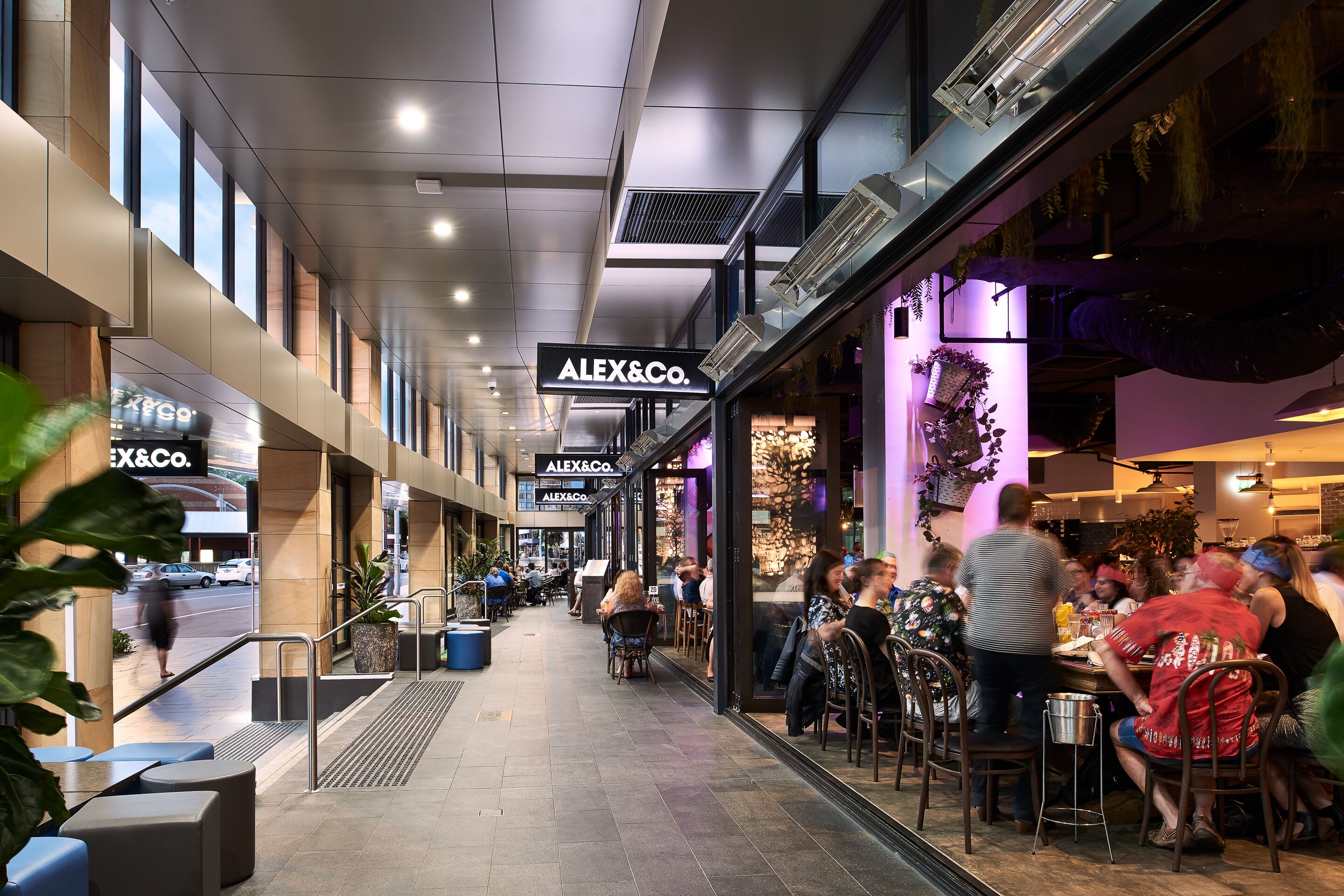 Un centre commercial moderne qui abrite un restaurant appelé « ALEX&Co. » et où l’on peut voir un escalier mécanique.
