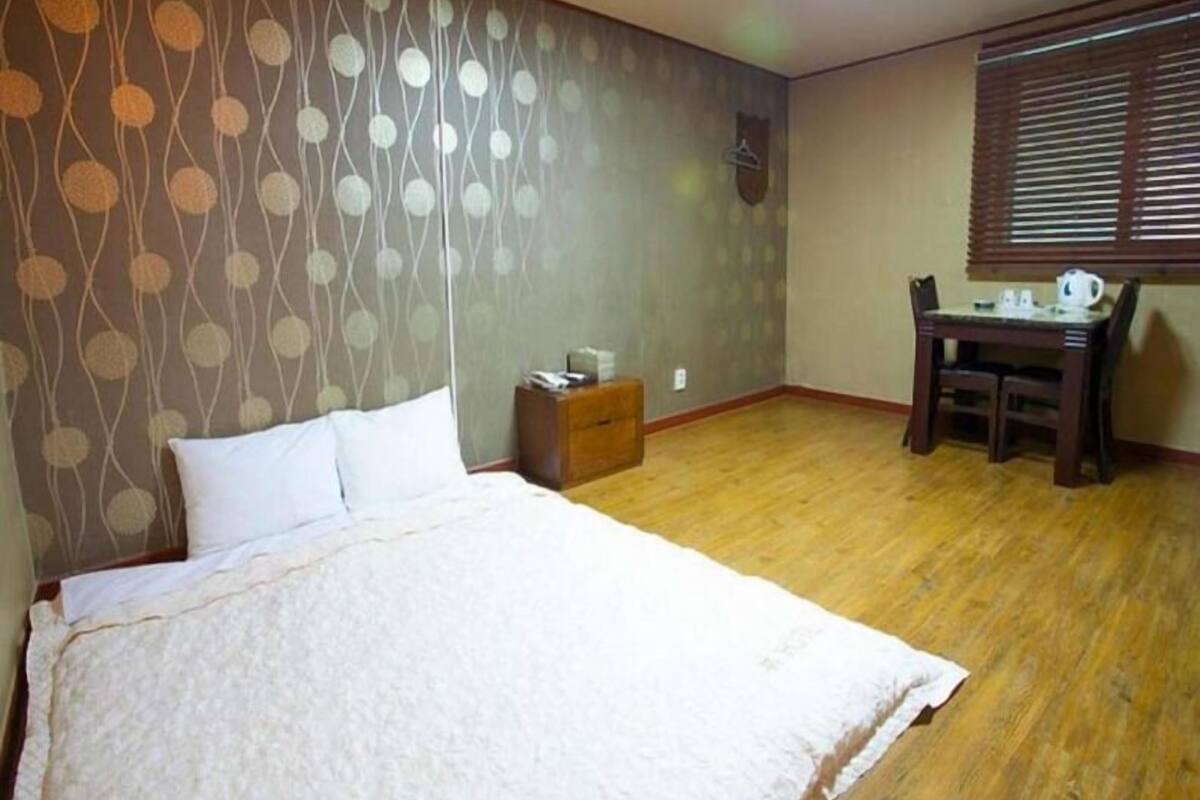 Un dormitorio con una cama, un aparador de madera, un escritorio con una silla y una ventana con persianas.