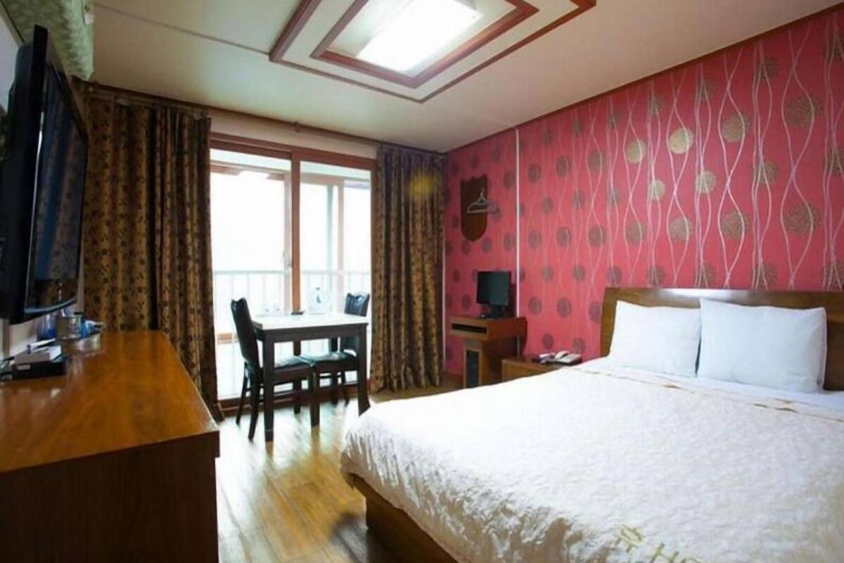 Una habitación de hotel con cama, escritorio, silla, televisor y ventana con cortinas.