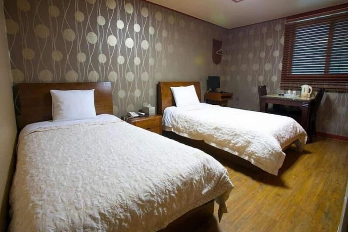 Habitación de hotel con dos camas, un escritorio y una ventana con persianas.