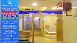 Ein Hotel Eingangsbereich mit einer Rezeption, einem Schild mit 'Check In Room.com' und einer Auflistung von Dienstleistungen wie Flugtickets, Autovermietung und einer kostenlosen Touristkarte.