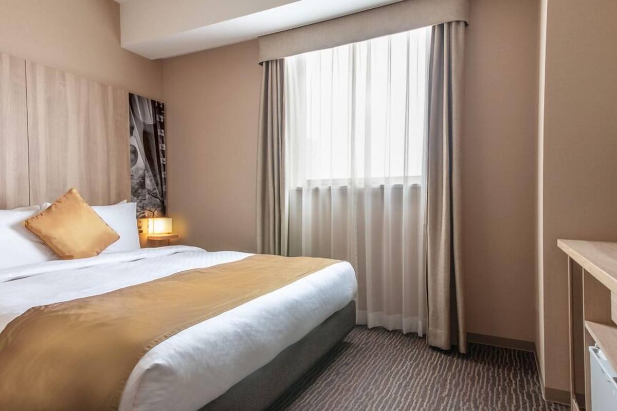 A hotel room with a bed, a nightstand, a lamp, and a window with curtains.