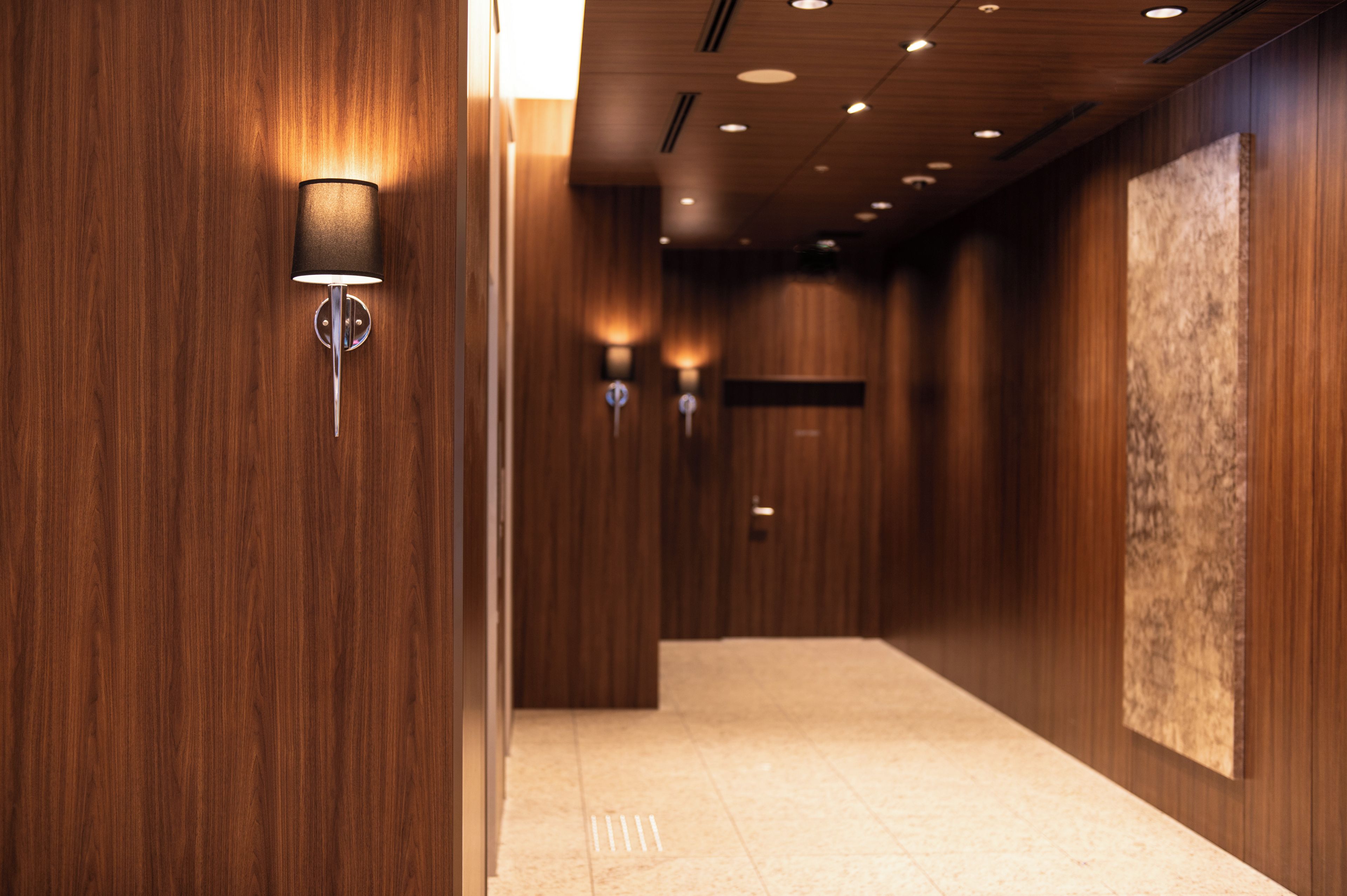 A corridor with wooden walls, recessed ceiling lights, and a large abstract painting on the right.