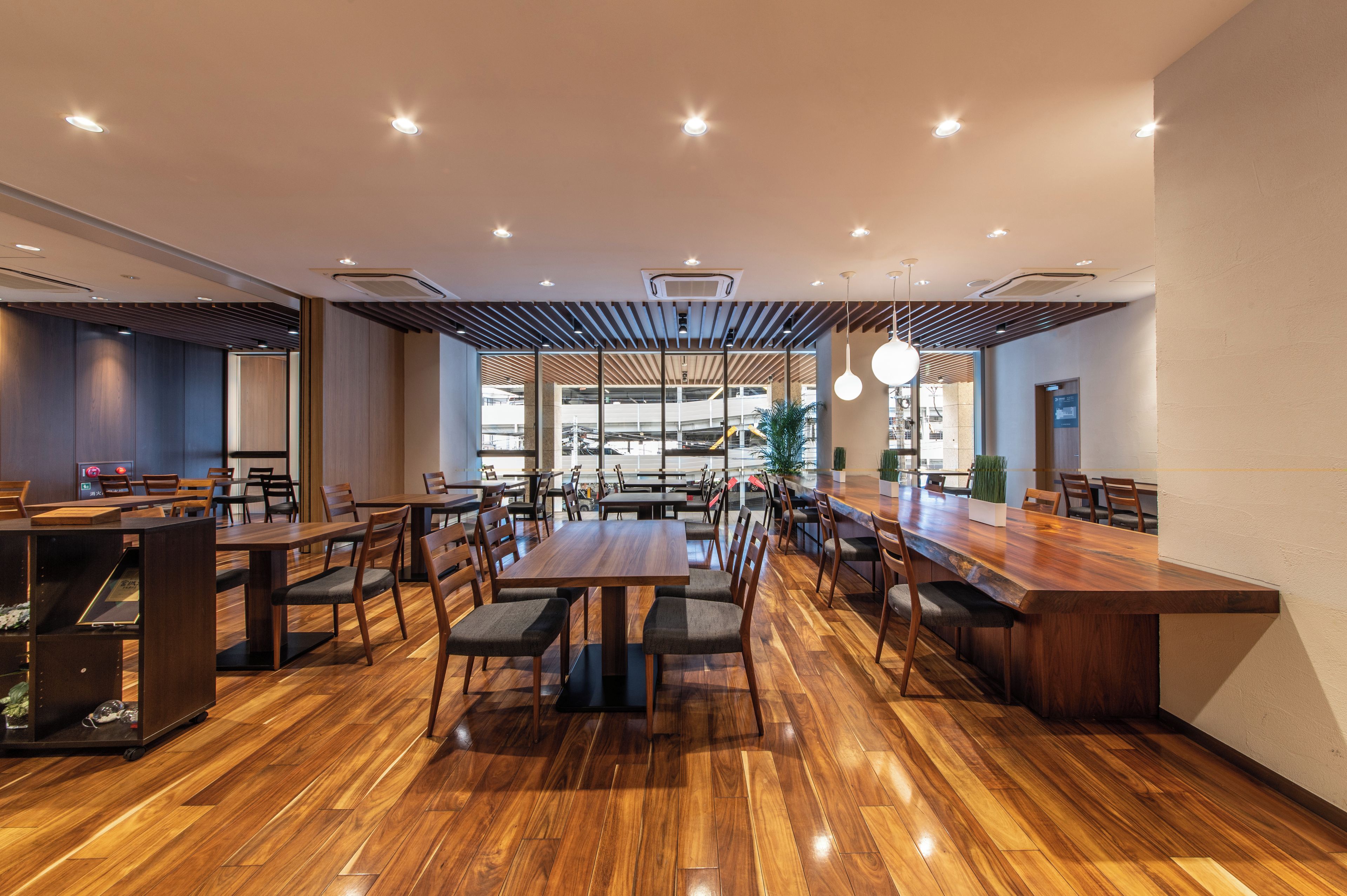 A spacious restaurant with wooden flooring, multiple tables and chairs, and a modern ceiling design.