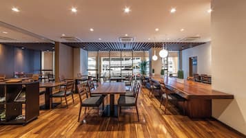 A spacious restaurant with wooden flooring, multiple tables and chairs, and a modern ceiling design.