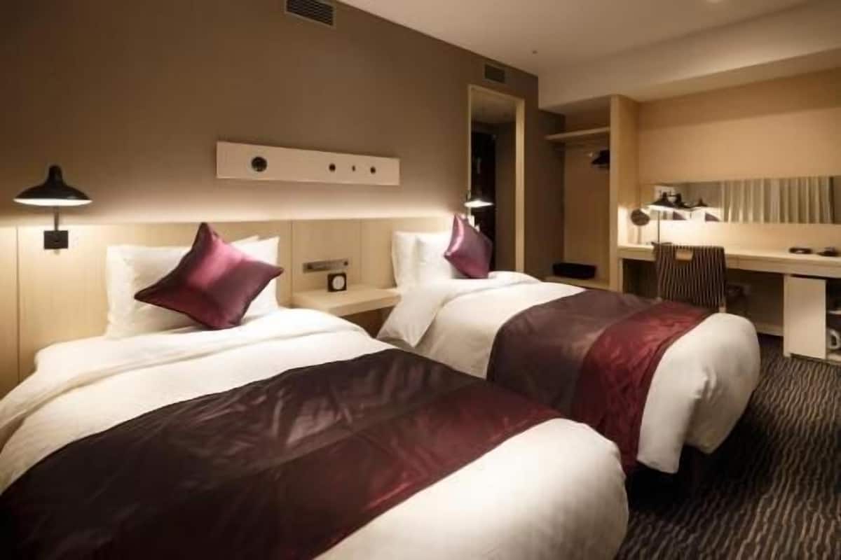 A hotel room with two beds, a desk, a chair, and a mirror.