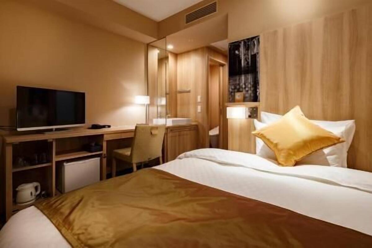 A hotel room with a bed, a desk with a TV, a chair, and a wardrobe.