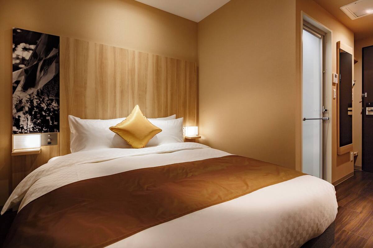 A hotel room with a large bed, wooden headboard, bedside lamps, and a door to the right.