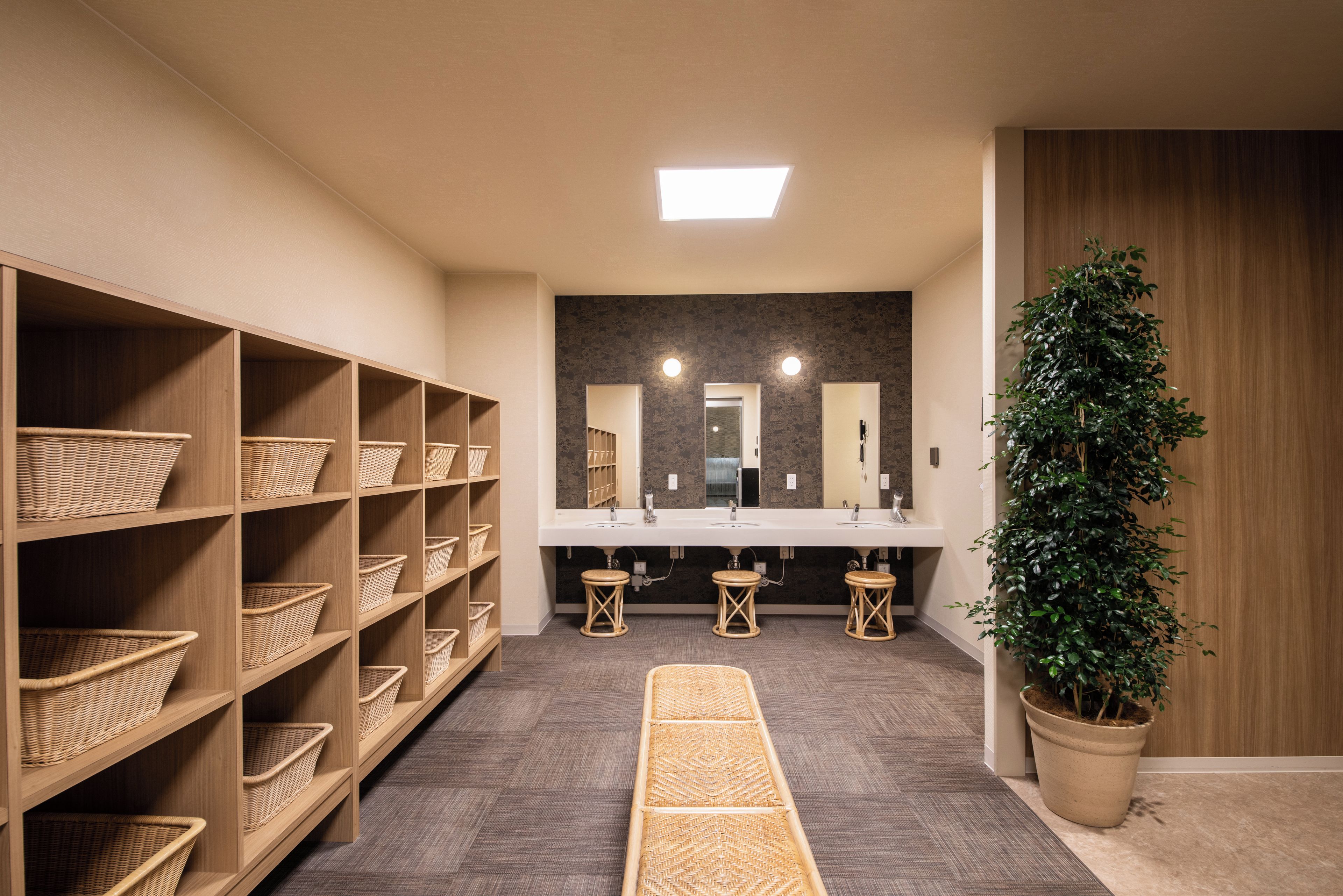 Un baño moderno con estantes de madera, cestas de mimbre, un espejo central y una planta en maceta.