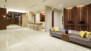 A modern hotel lobby with a reception desk, bar area, and seating with a patterned sofa and a tall vase. - Hotel Vista Sendai (Sendai)