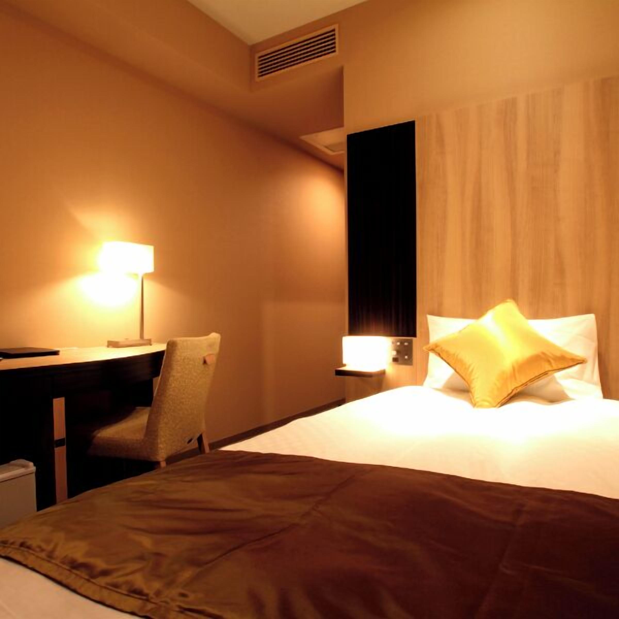 Une chambre d’hôtel avec un lit, un bureau, une chaise et une lampe.