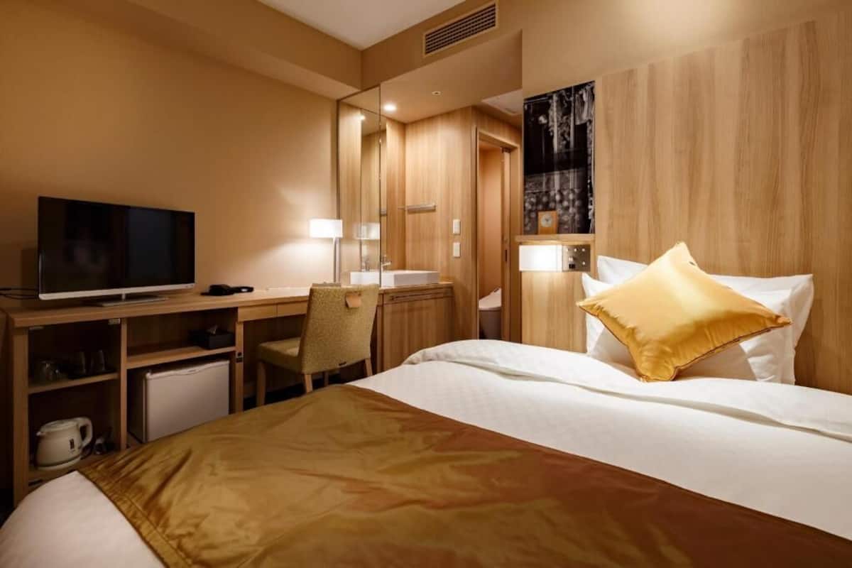 A hotel room with a bed, a desk, a chair, a television, and a mirror.