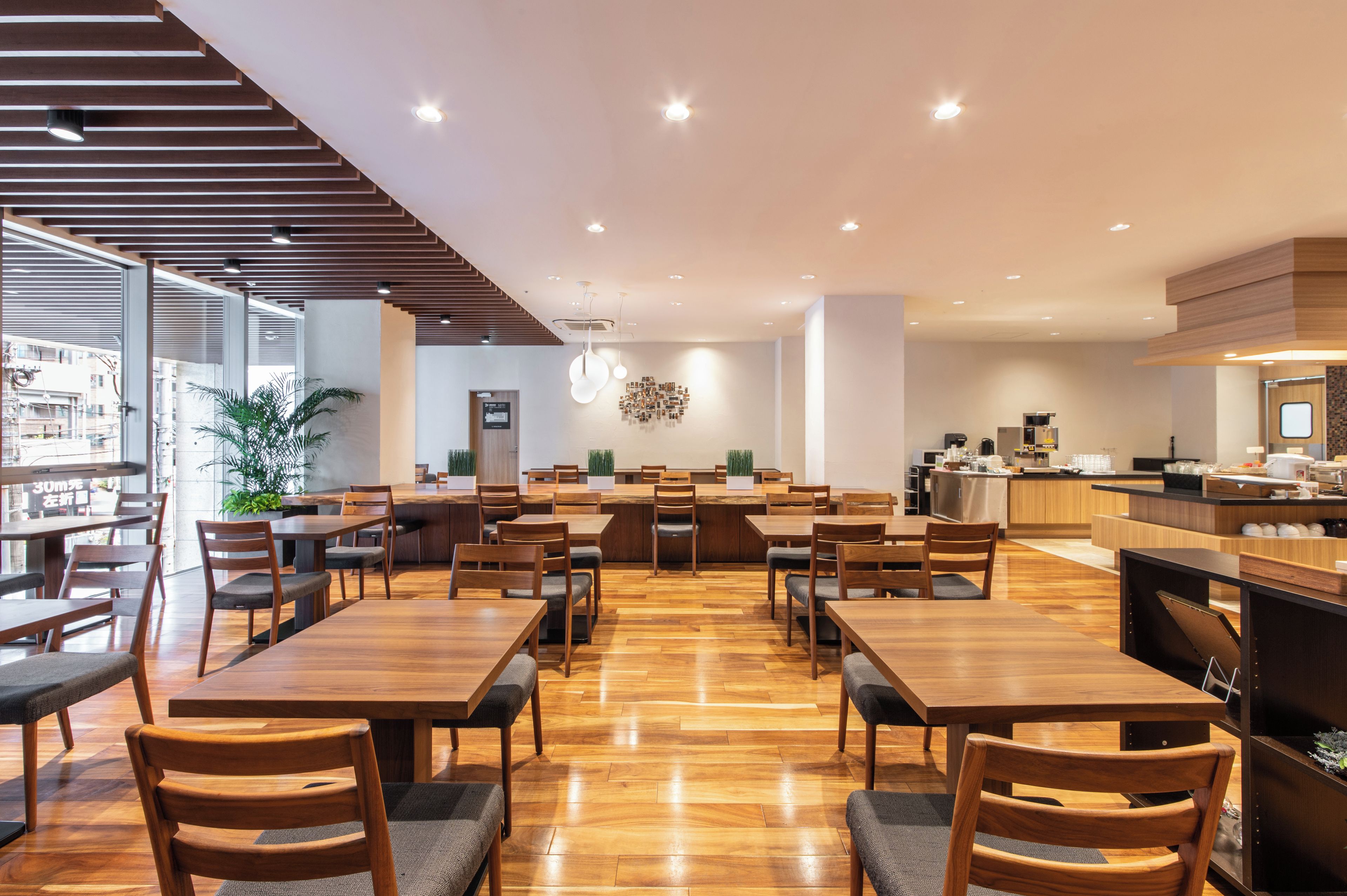 Un restaurant spacieux avec des tables et des chaises en bois, un espace cuisine et une vue sur l’extérieur.