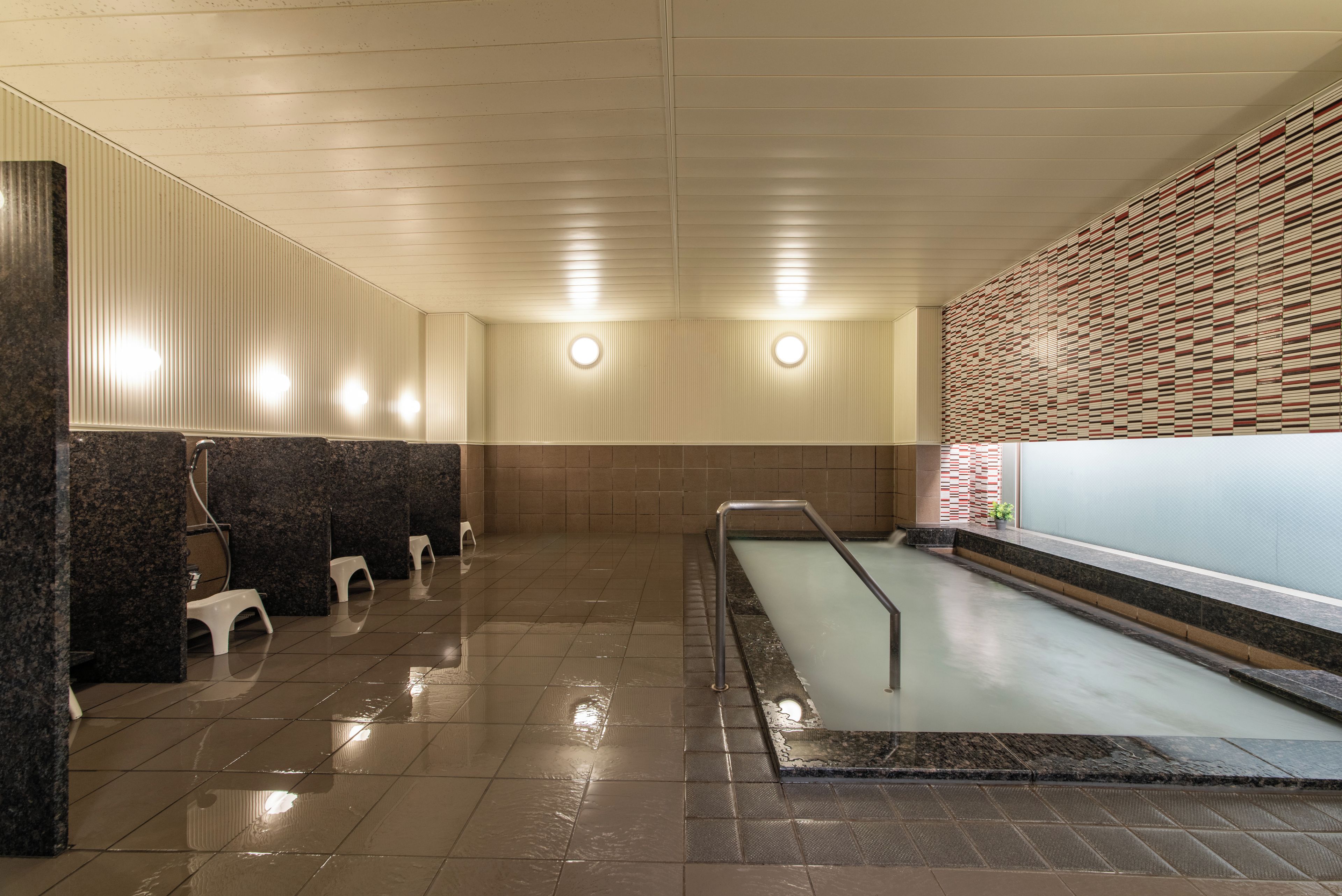 Une salle de bain propre et moderne, avec un sol carrelé, un espace détente avec des tabourets et un mur orné d'un motif texturé.