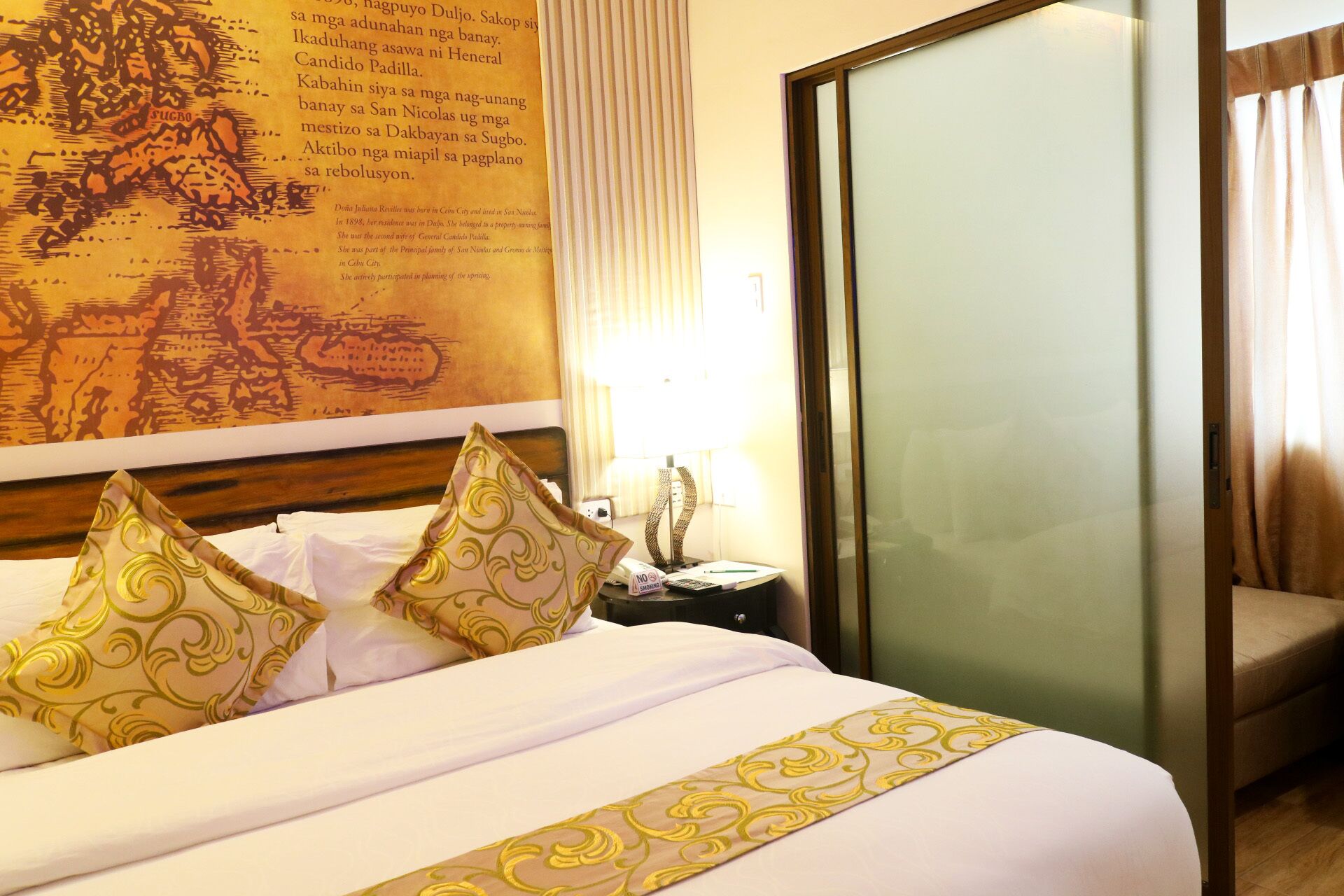 Une chambre d’hôtel avec un grand lit, deux coussins décoratifs, une table de chevet avec une lampe et une grande carte encadrée accrochée au mur.