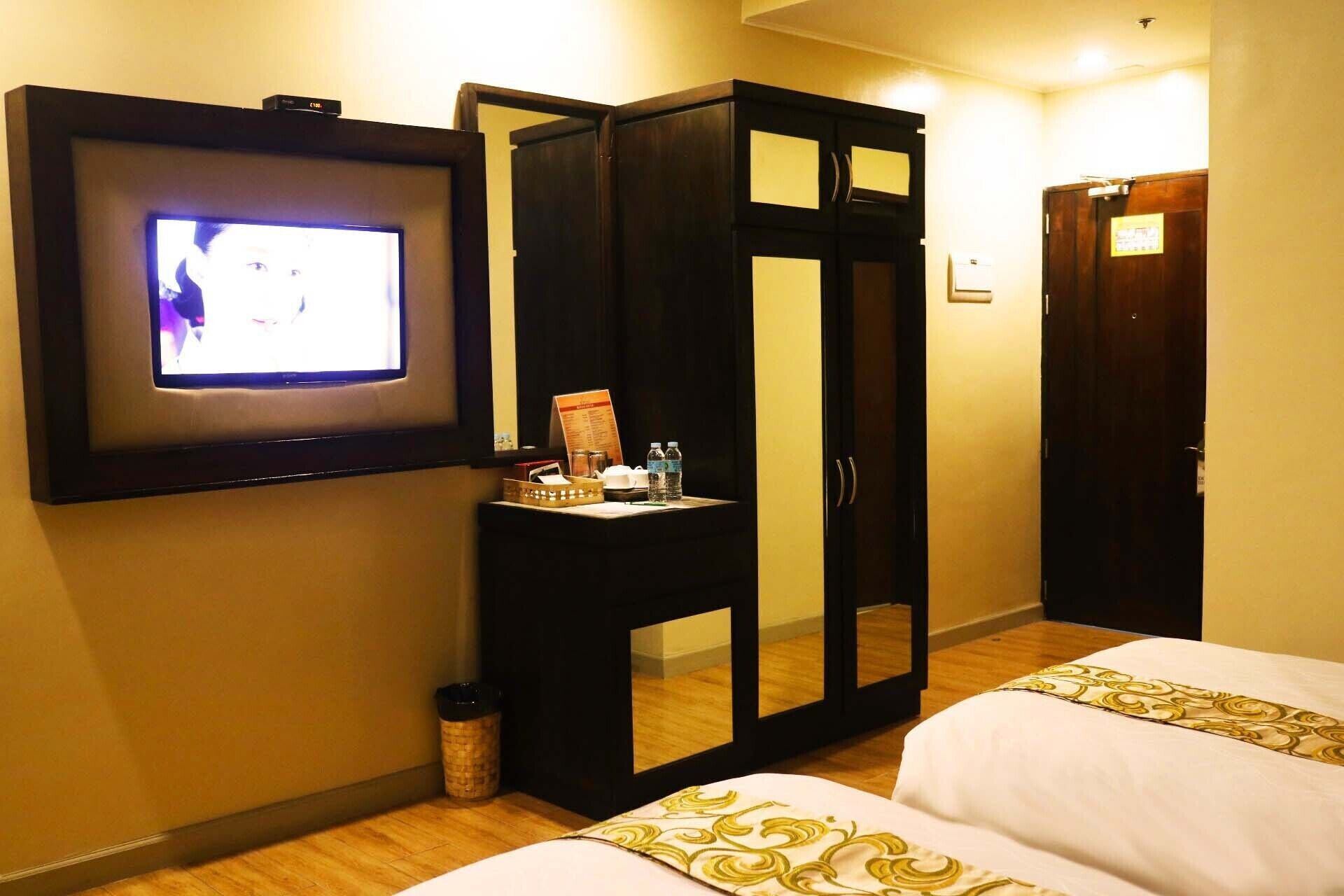 Une chambre d’hôtel dotée d’un téléviseur fixé au mur, d’une armoire aux portes miroir et de deux lits avec du linge de lit blanc.