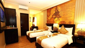 A hotel room with two beds, a large map on the wall, a TV, and a desk with a lamp.