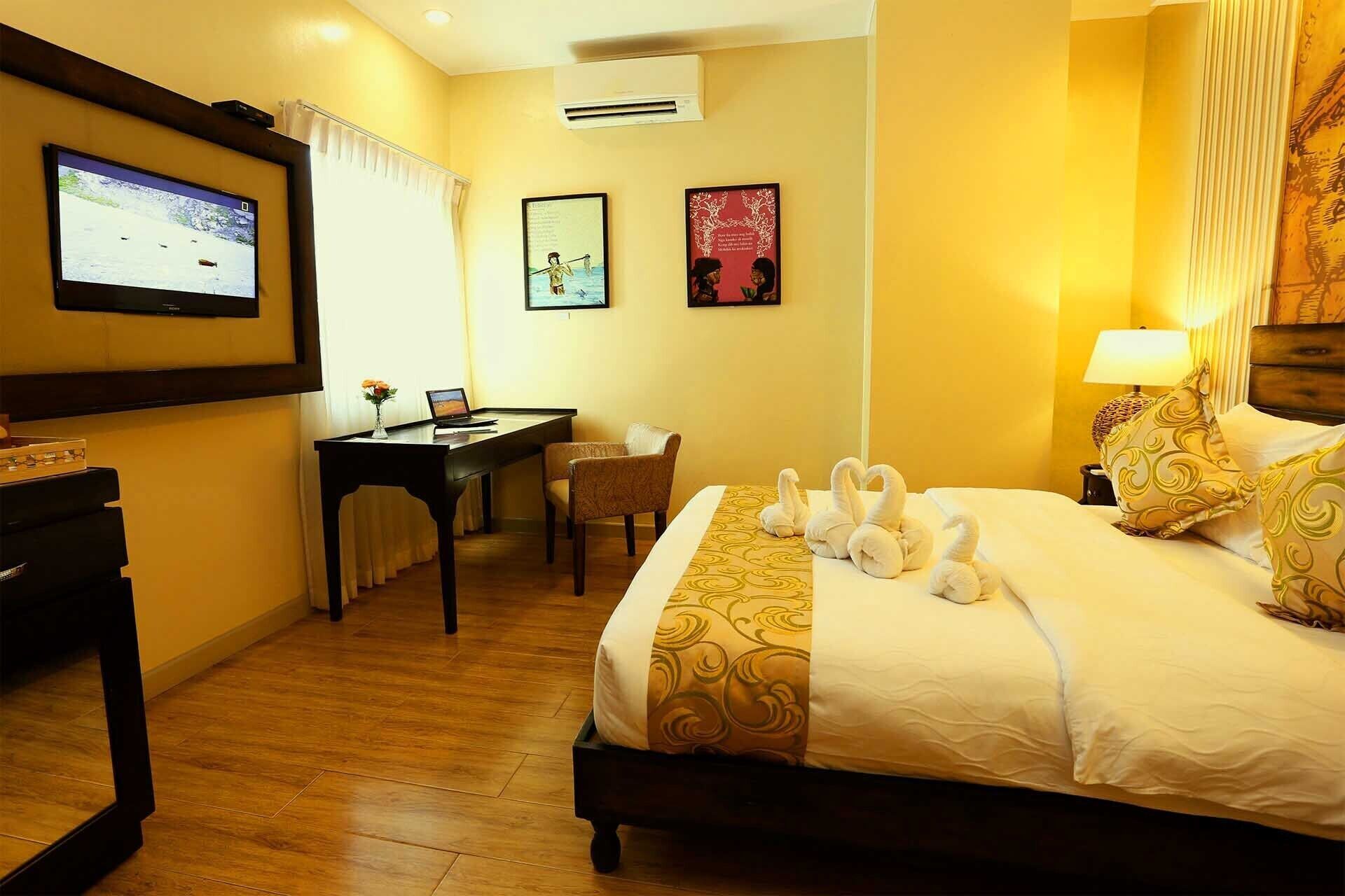 A hotel room with a bed, a desk, a chair, a TV, and a wall-mounted air conditioner.