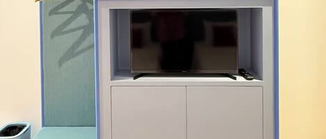 Una habitación con televisión integrada, un estante pequeño y un perchero.