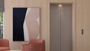 Un moderno vestíbulo con un cuadro abstracto grande, una mesa redonda, dos sillones cómodos y un ascensor.