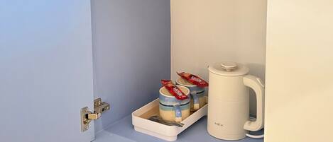 A kitchen area with a blue wall, a white cabinet, and a coffee maker.