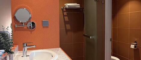 A modern bathroom with a white sink, a round mirror, and a glass shower enclosure.
