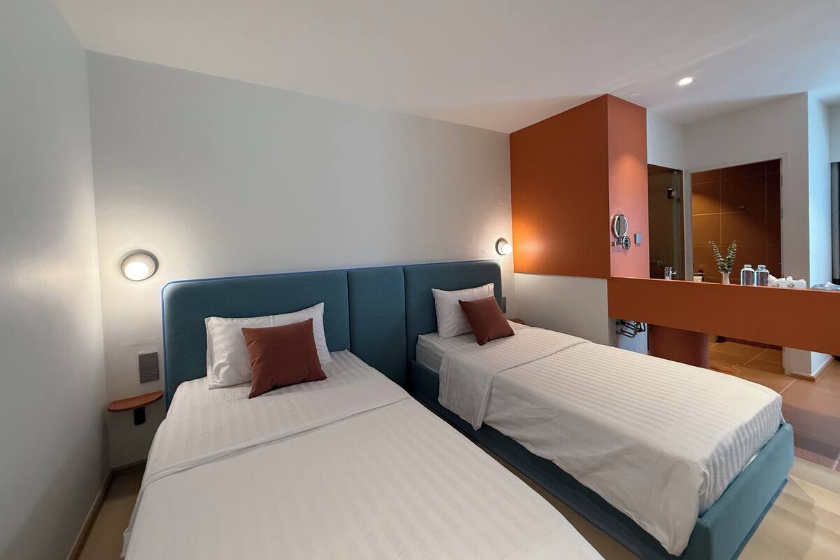 Habitación de hotel con dos camas, baño y una pequeña zona de estar.