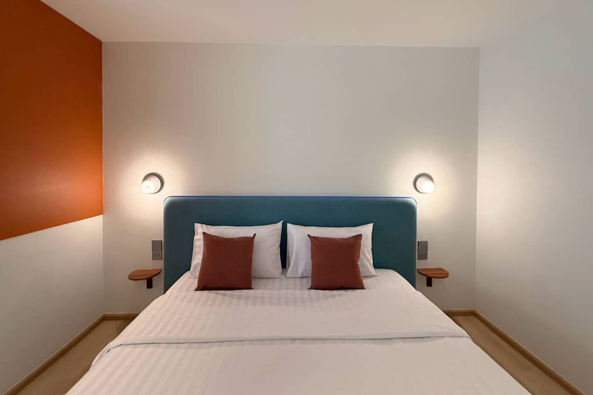 Una cama bien hecha con un cabecero azul, dos mesitas de noche y dos lámparas de pared.