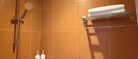 A bathroom with a shower, a towel rack, and two bottles of shampoo.