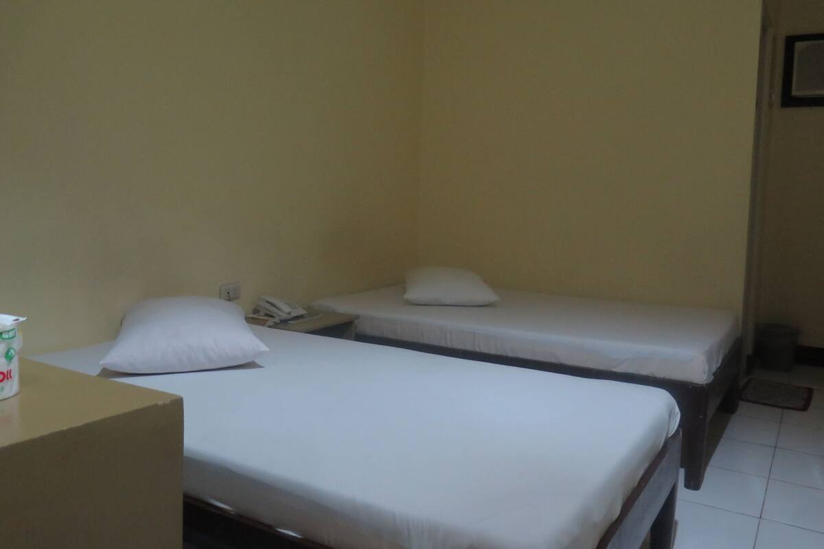 A small, simple room with two single beds, a bedside table, and a wall-mounted telephone.