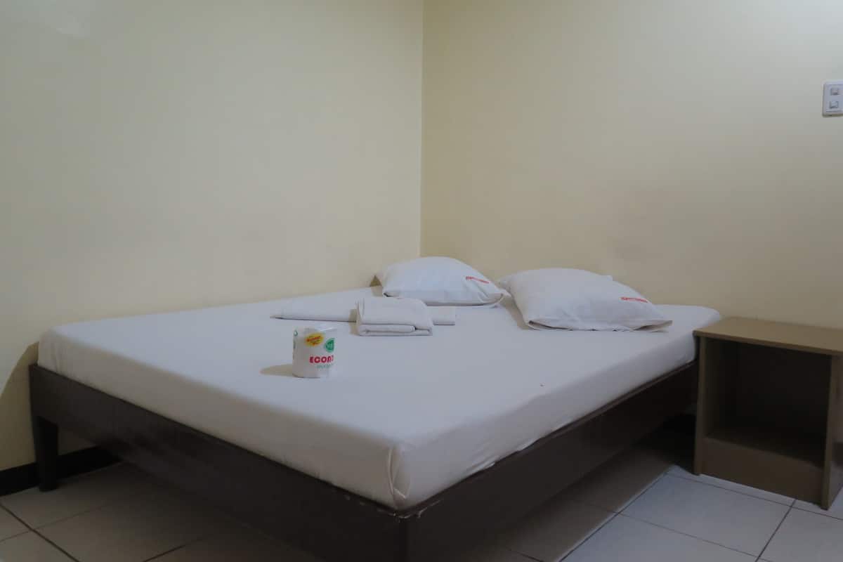 A single bed with white linens, pillows, and a bottle of Ecover dish soap.