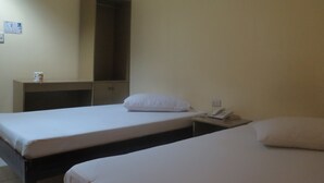 Une chambre avec deux lits simples, une armoire, une table de chevet avec un téléphone et une petite étagère avec une boîte de conserve.