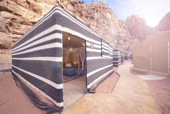 A series of striped tents with a visible room containing a bed and a small table.