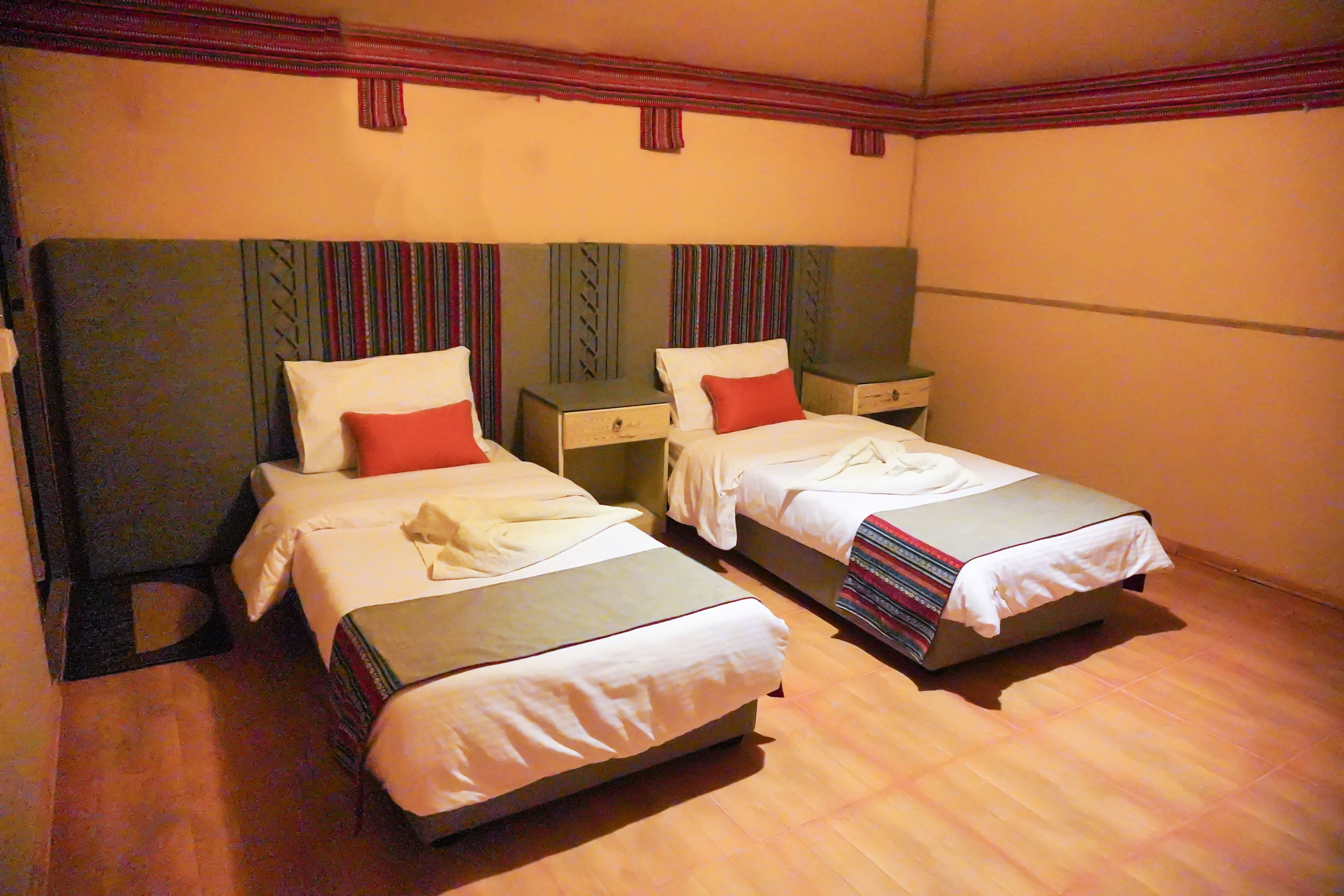 Ein Hotelzimmer mit zwei Einzelbetten, jeweils mit Kissen und Decke.