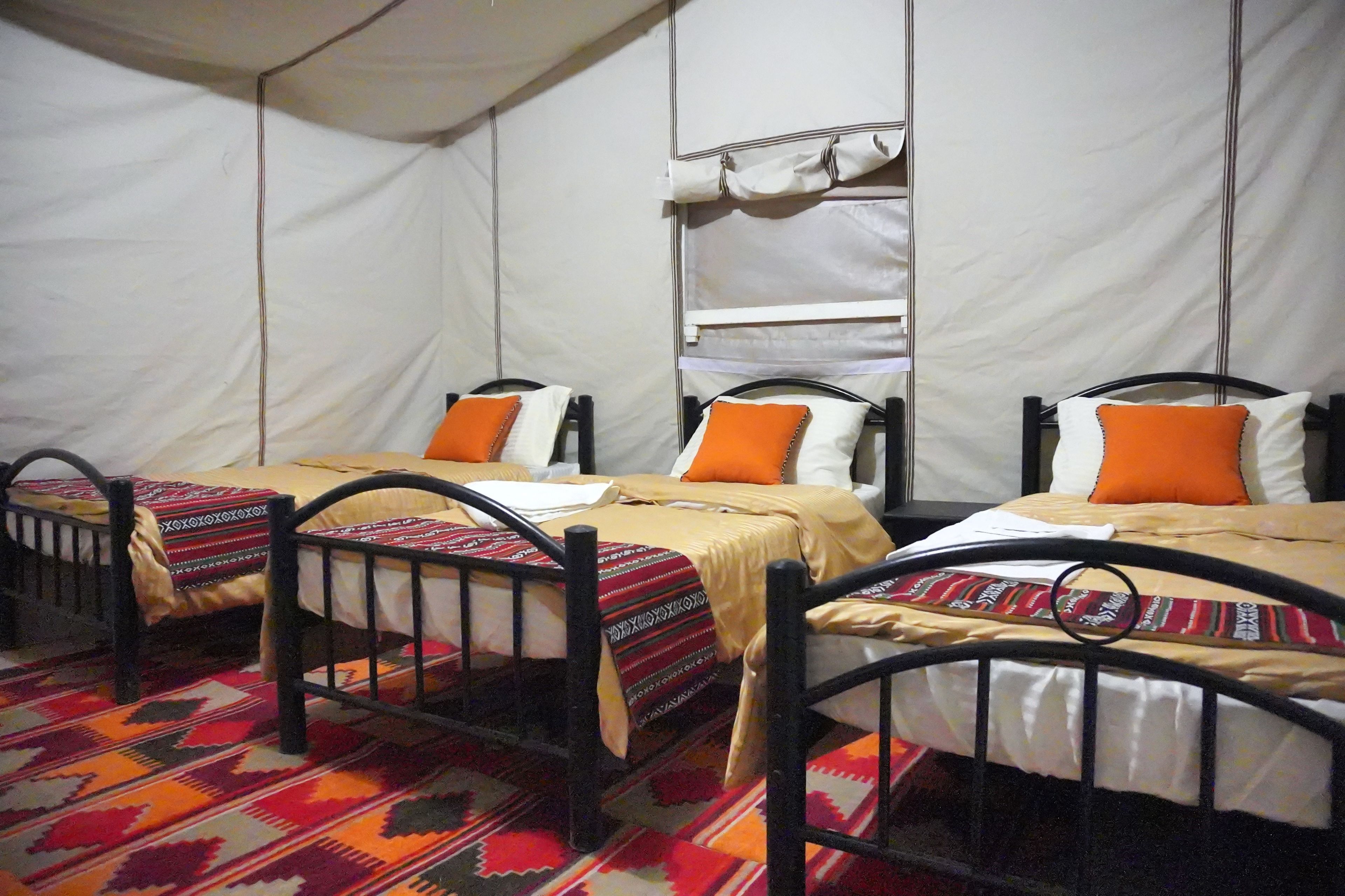 Three single beds with black frames and white bedding, arranged in a row with a patterned carpet.