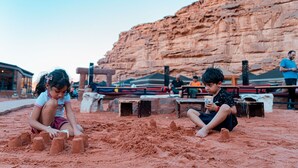 Bambini che giocano con la sabbia in uno spazio aperto con uno sfondo roccioso.