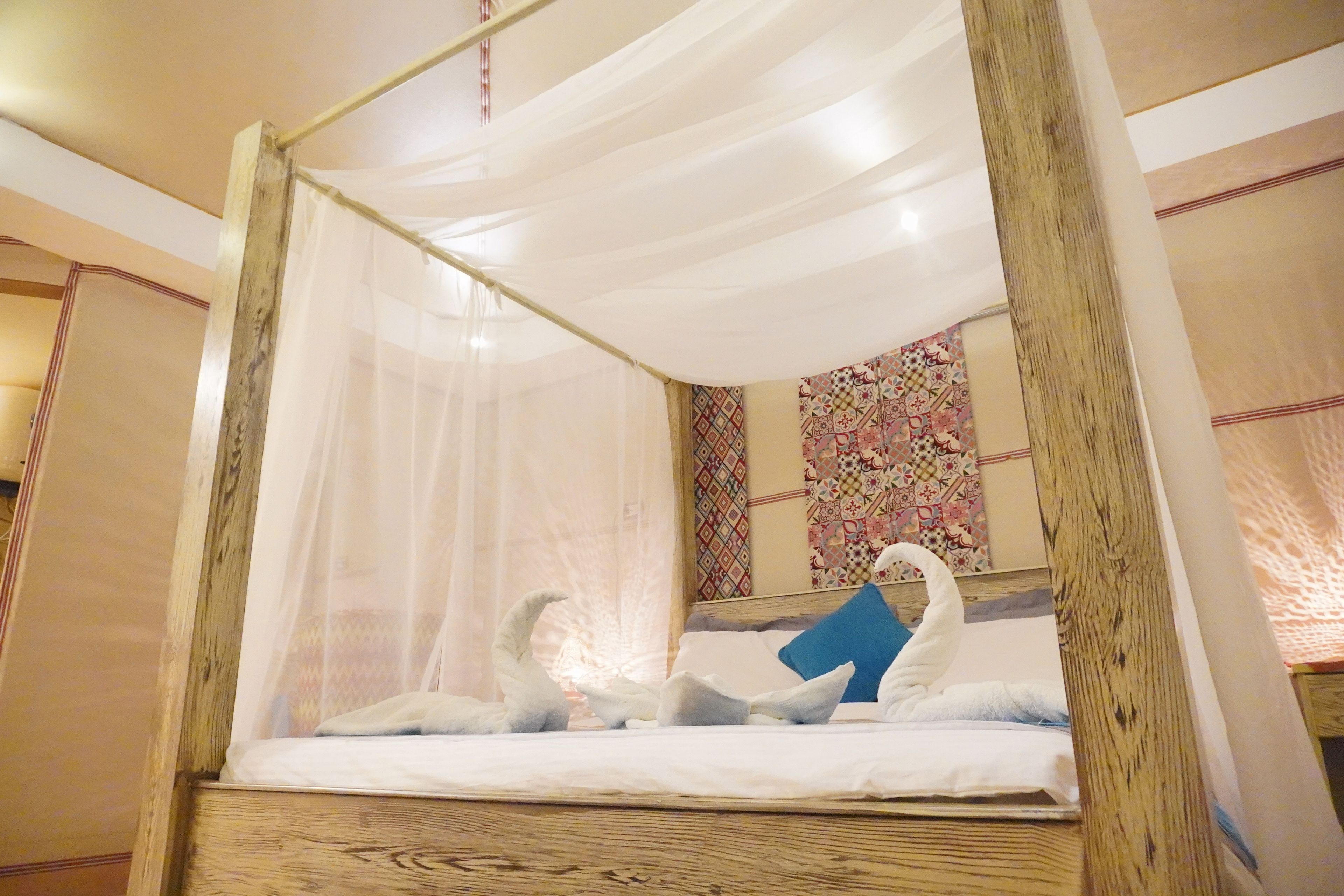 A four-poster bed with a canopy, a blue pillow, and a decorative swan pillow.