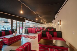 A restaurant with red and black upholstered booths, a long counter, and hanging lights. - Rahayeb Desert Camp (Wadi Rum)