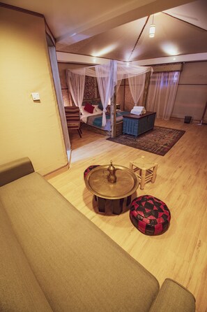 A cozy room with a sofa, a round table with a brass pitcher, and a patterned ottoman. - Rahayeb Desert Camp (Wadi Rum)
