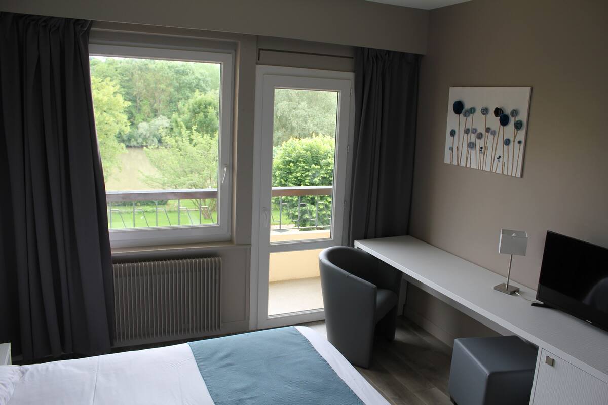 Une chambre d’hôtel équipée d’un lit, d’un bureau, d’une chaise, d’une télévision et d’une fenêtre avec des rideaux.