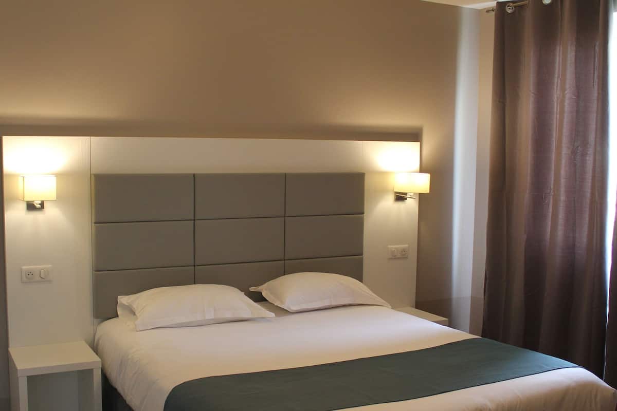 Une chambre d’hôtel avec un lit, deux lampes de chevet, une table de nuit et un rideau.