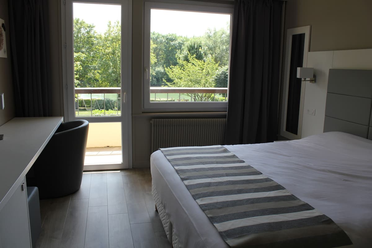Une chambre d’hôtel avec un lit, un bureau et une vue sur la verdure.