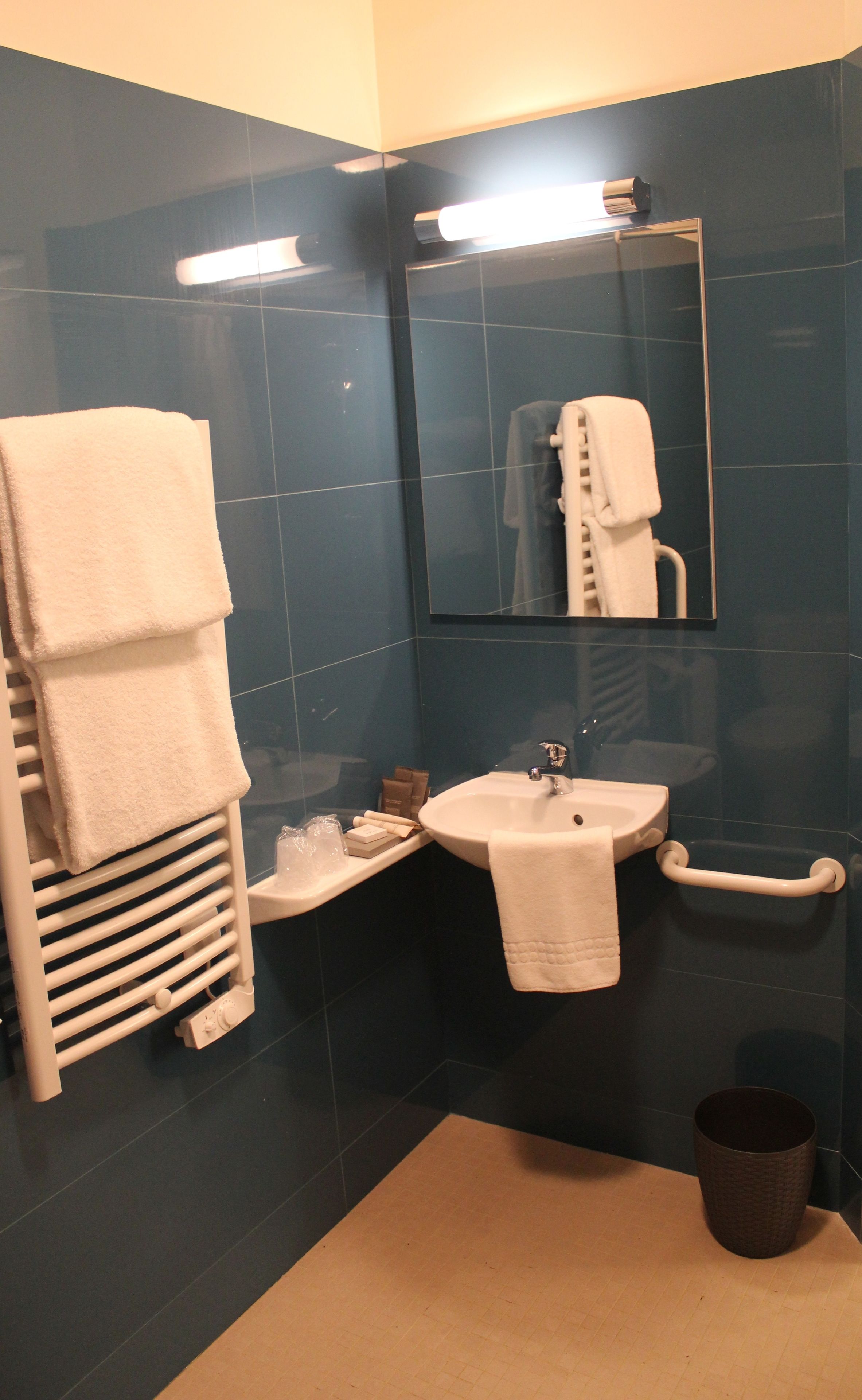 A bathroom with a sink, mirror, towel rack, and a trash bin.