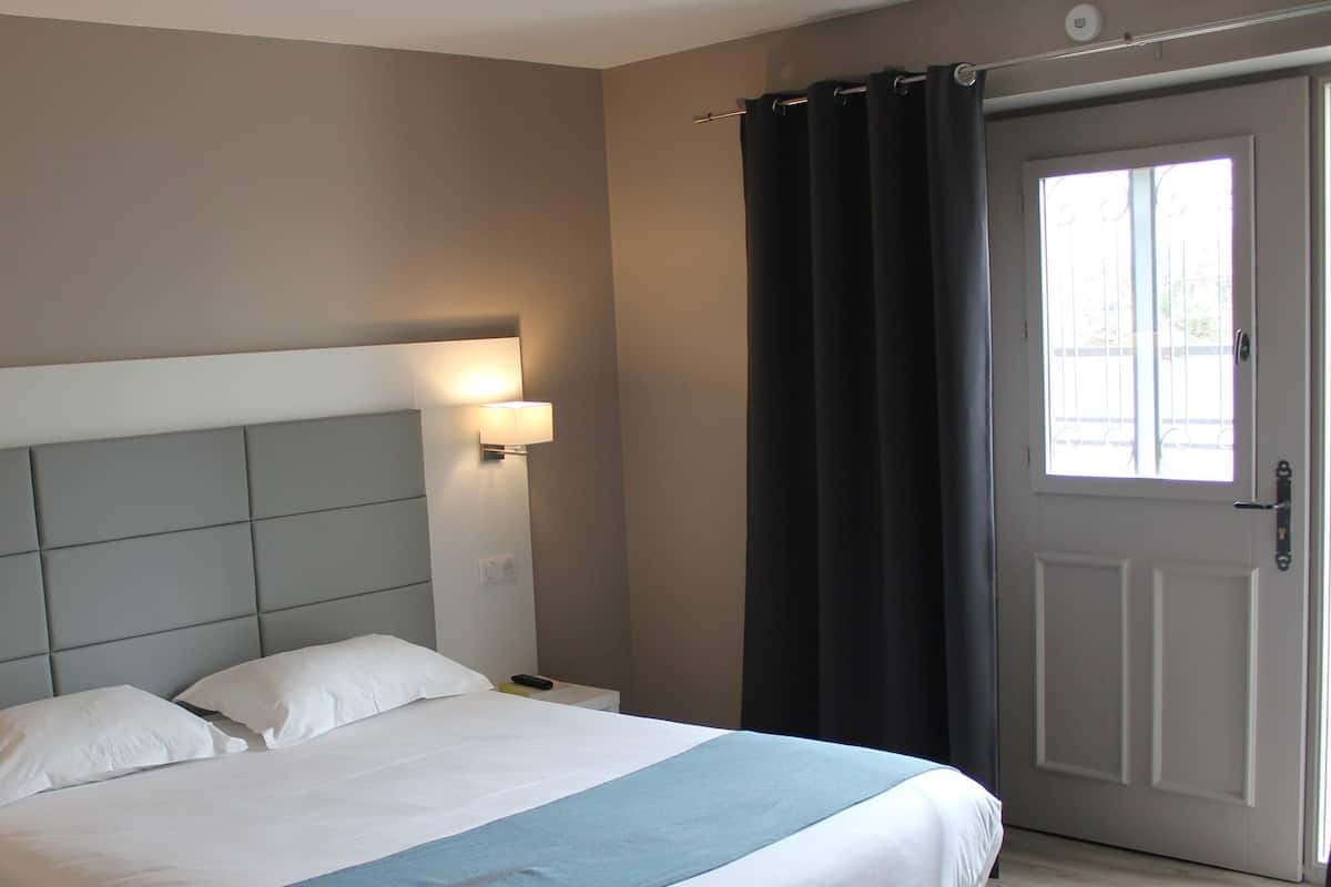 Une chambre d’hôtel avec un lit, deux lampes de chevet, une porte avec des rideaux et une prise électrique au mur.