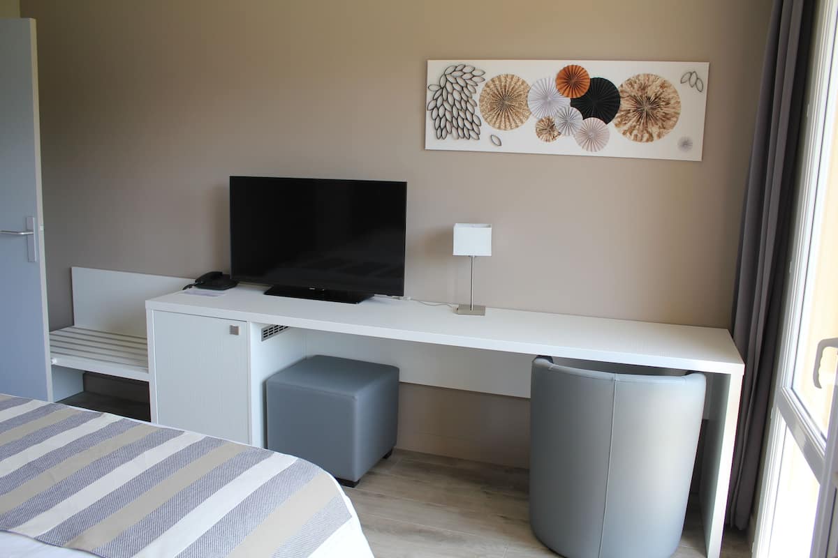 Une chambre d’hôtel comprenant un lit, un bureau avec un téléviseur à écran plat, une lampe et une œuvre d’art murale.