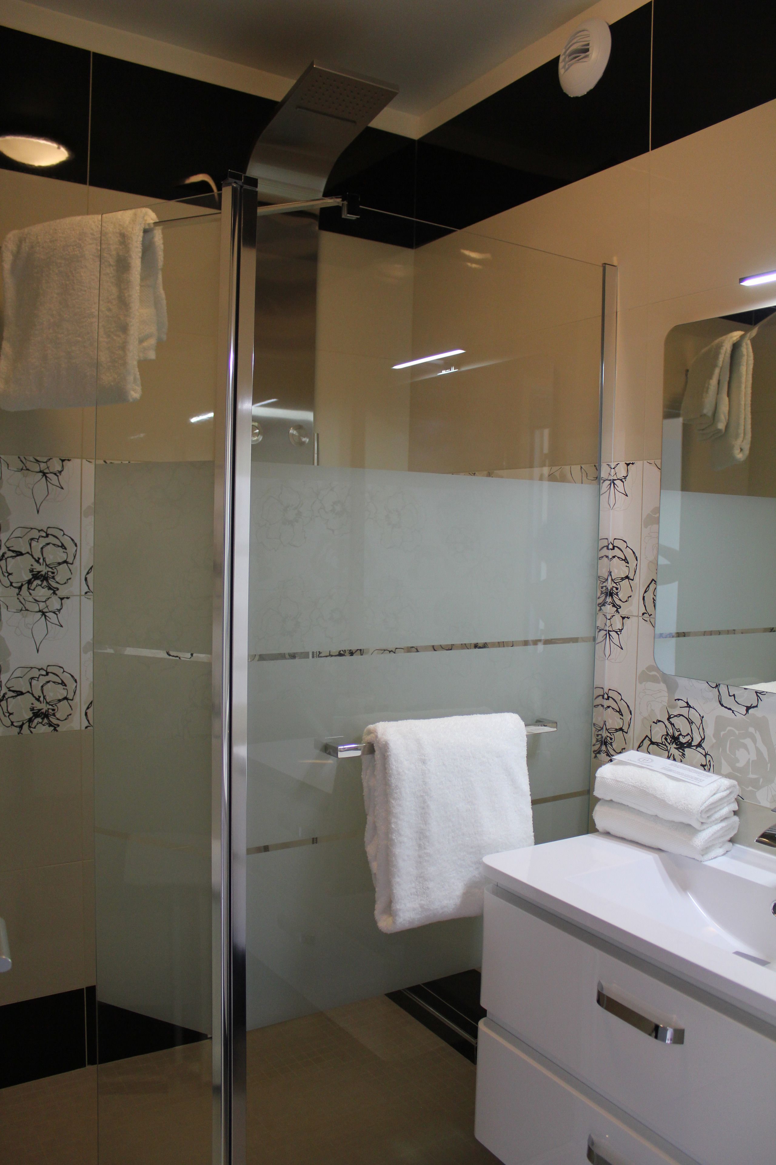 Un baño moderno con ducha envuelta en vidrio, un tocador blanco con espejo y un perchero para toallas.