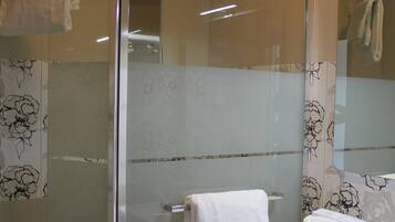 Un baño moderno con ducha envuelta en vidrio, un tocador blanco con espejo y un perchero para toallas.