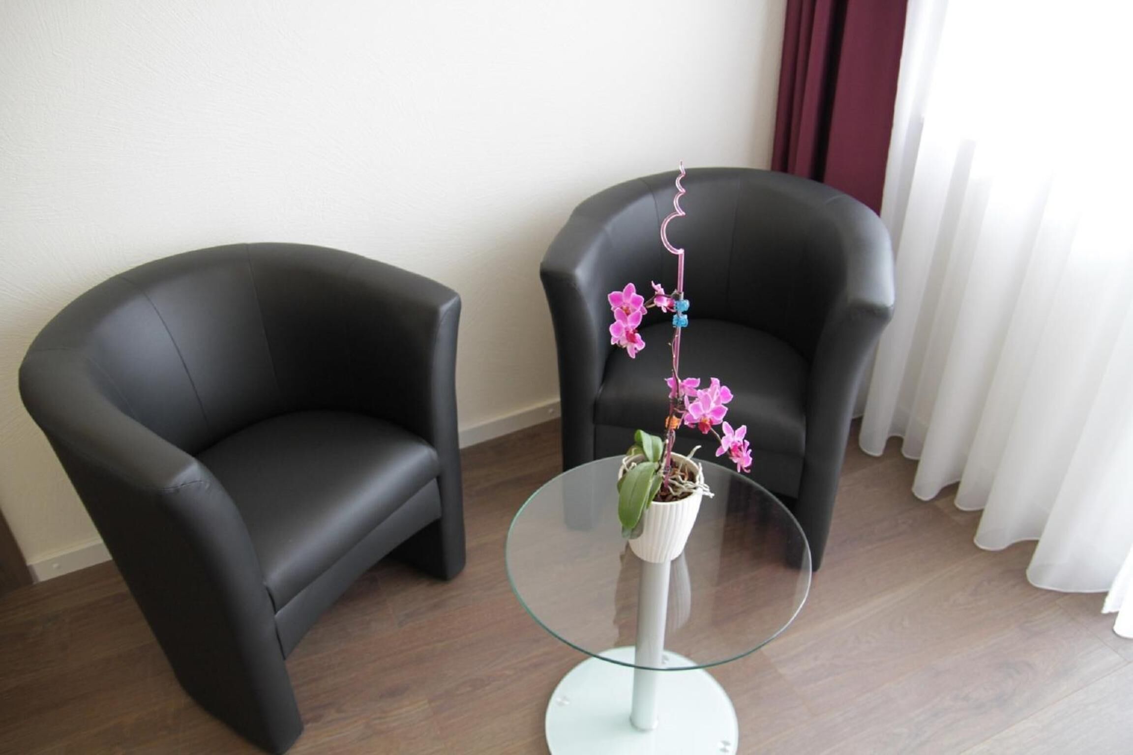 Una habitación con dos sillones de cuero negro y una mesa de centro de vidrio con una orquídea en maceta.