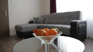 Una sala de estar moderna con una mesa de vidrio que sostiene fruta, un sofá gris y una puerta de madera.