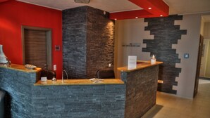 Un área de recepción con mostrador de piedra, escritorio de madera y pared decorativa roja.